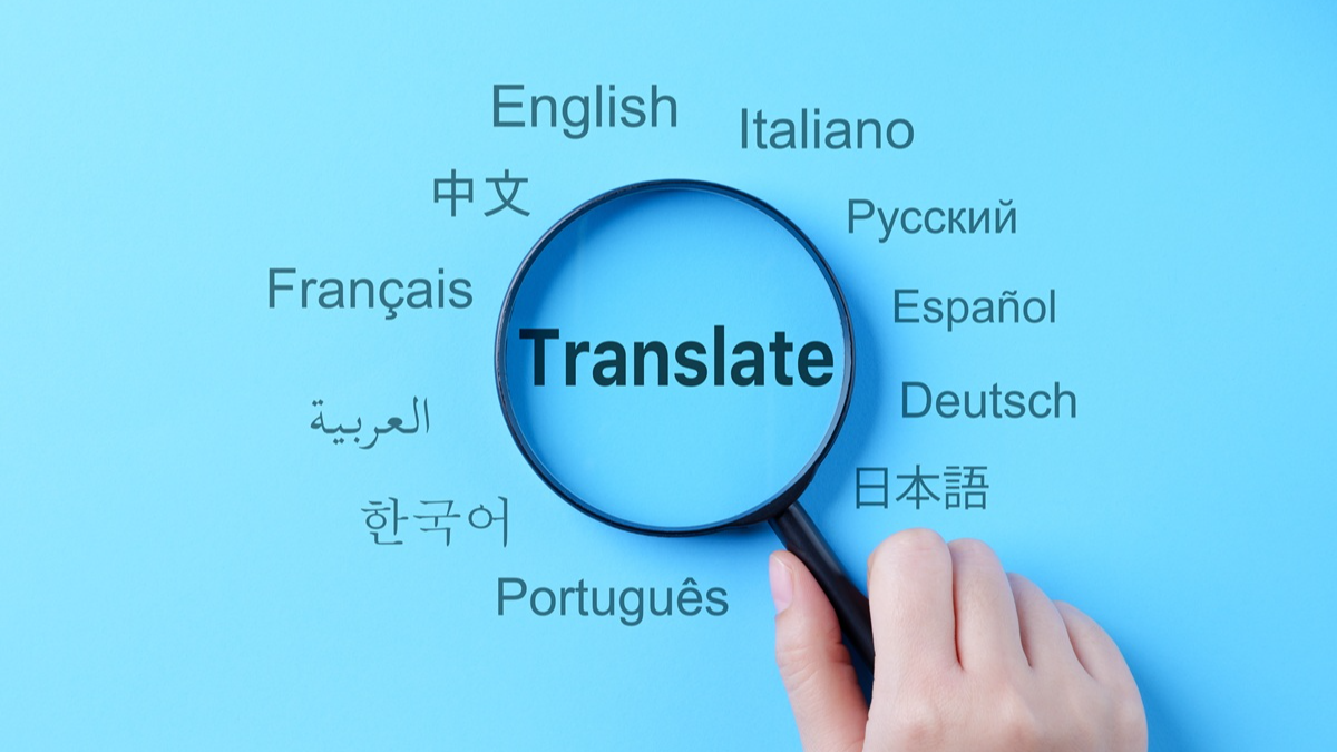 Hand holding a magnifier on the word "Translate" in the middle of several different languages